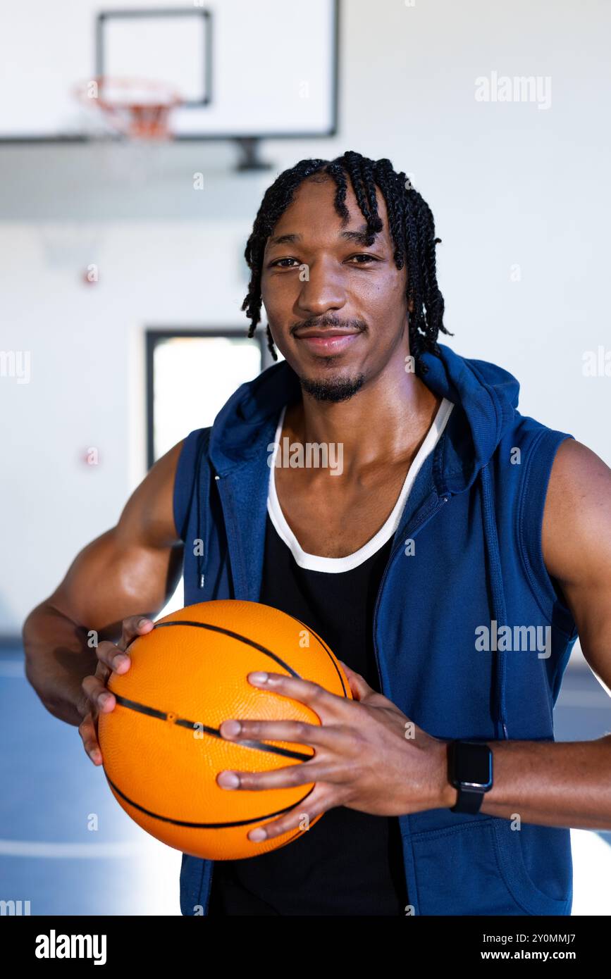 Tiene il basket, un afroamericano sorridente con fiducia nel campo da basket della scuola al coperto Foto Stock