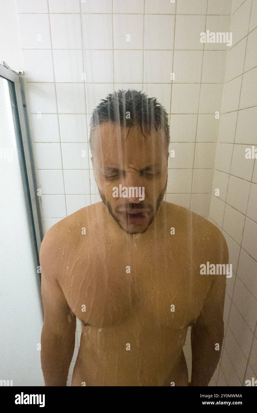 Un uomo è in piedi in una doccia con la testa sott'acqua. Indossa una camicia e ha la barba Foto Stock Un uomo è in piedi in una doccia con la testa sott'acqua. Indossa una camicia e ha la barba Foto Stock