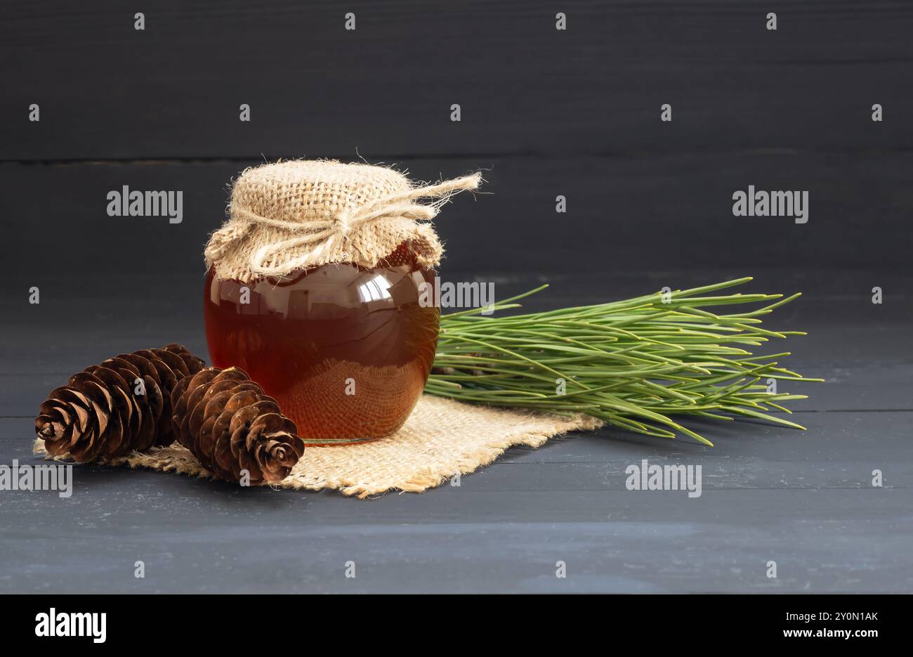 Miele di pino in vaso o ciotola con bastoncino di miele e coni di pino su tavola rustica di legno, cibo sano Foto Stock