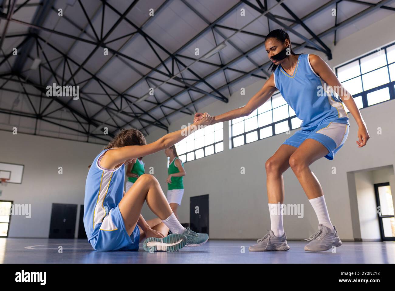 Aiuta la compagna di squadra ad alzarsi in piedi, giocatrici di basket femminili nella sala dello sport durante la partita Foto Stock