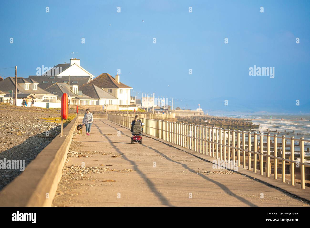 I turisti si godono il sole pomeridiano sulla parata marina/passeggiata a Tywyn Beach, Gwynedd, Galles, Regno Unito. Foto Stock