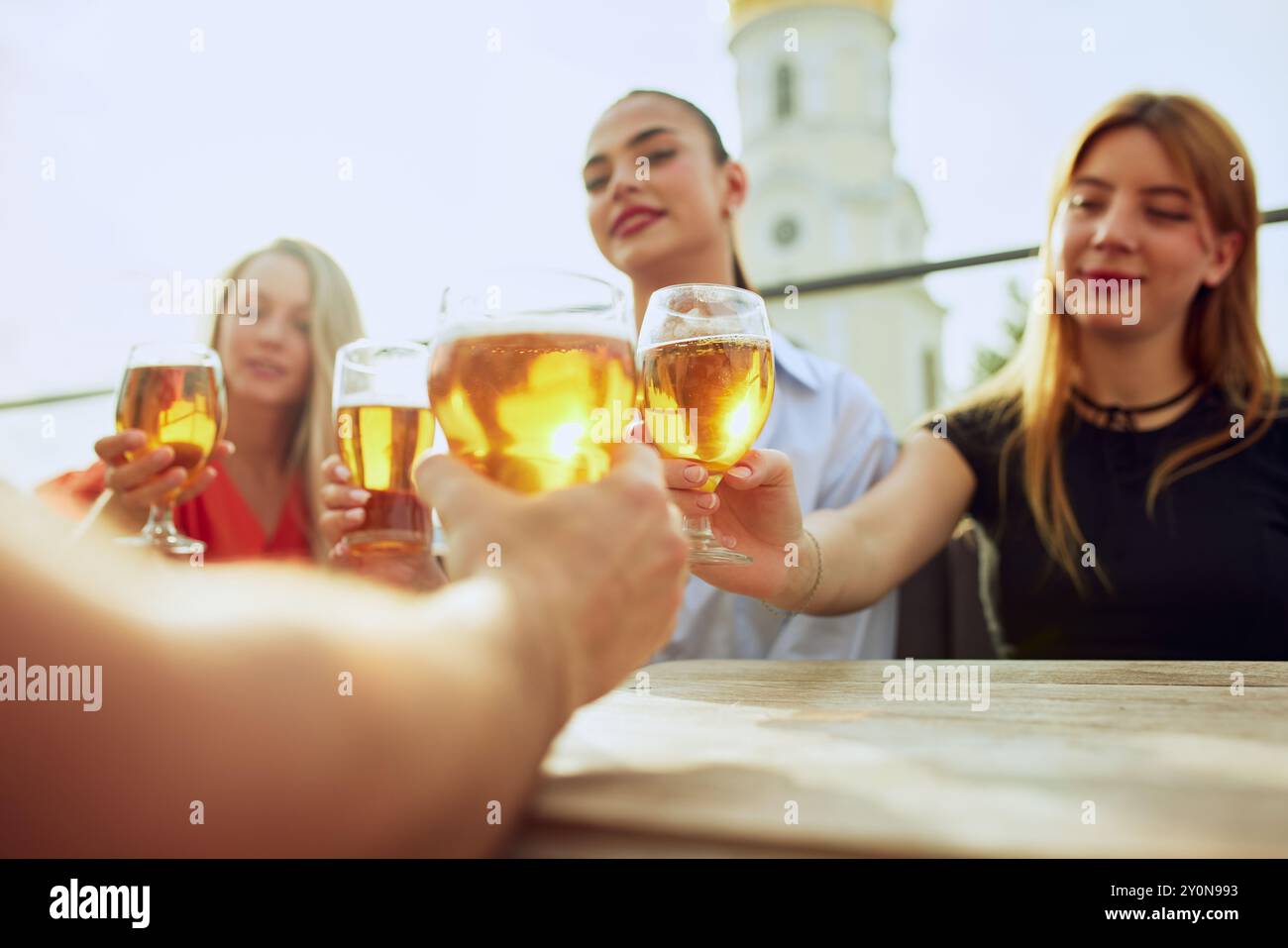 Circondata da amici, la donna in bianco condivide un brindisi di cuore, mentre tutti si uniscono alla celebrazione, creando ricordi con bevande e conversazioni. Foto Stock