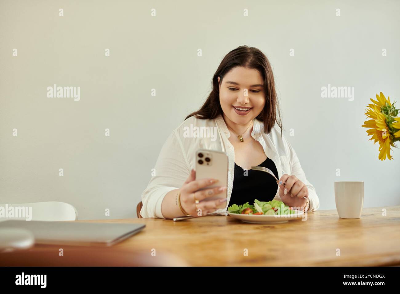 Una donna gioiosa gusta il suo delizioso pasto mentre si connette al telefono. Foto Stock