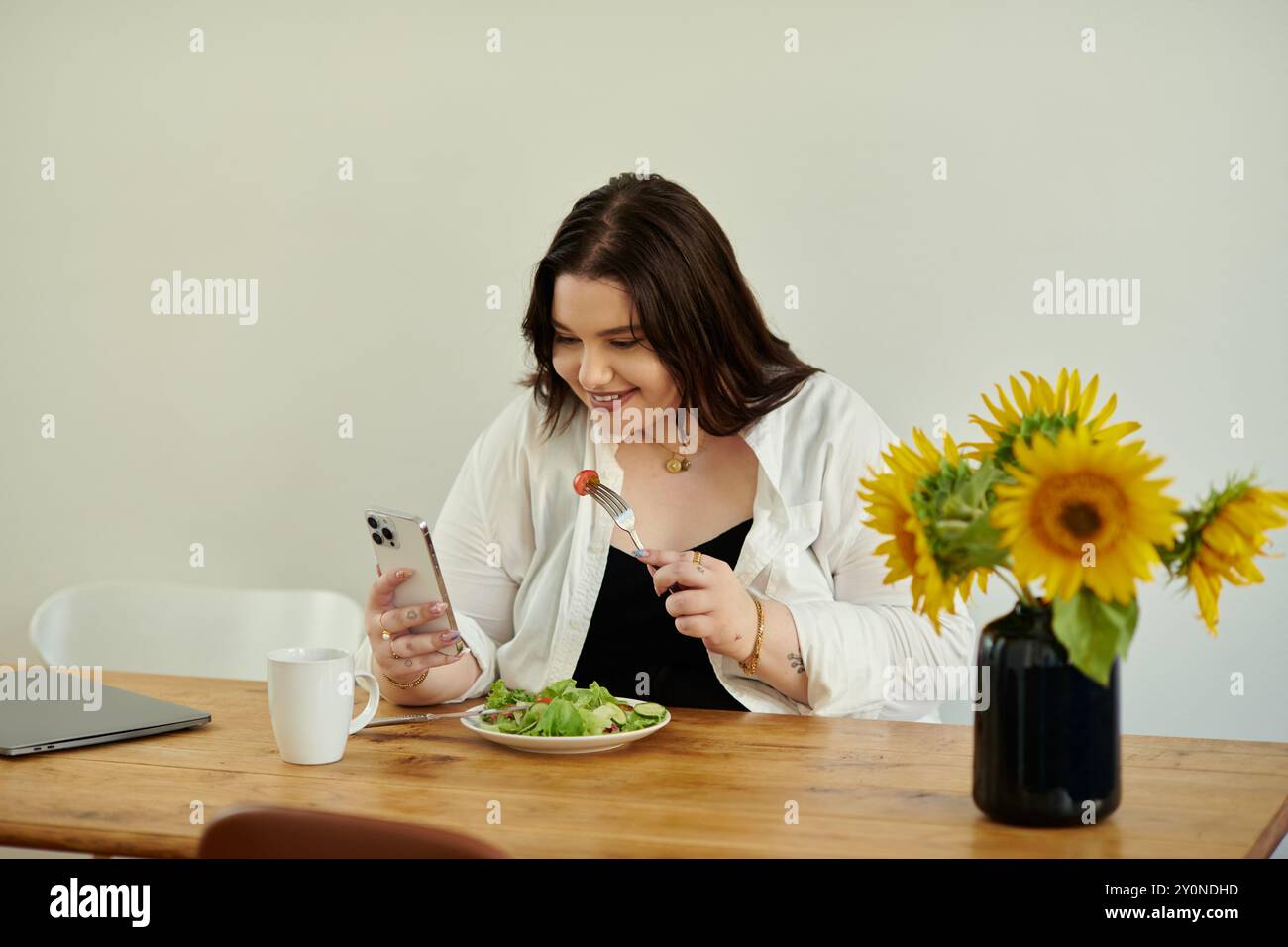 Una donna si delizia nel suo pasto mentre controlla il suo telefono, circondato da girasoli freschi. Foto Stock