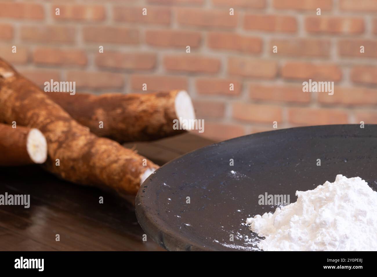 Amido di manioca all'interno di un piatto di argilla a destra dell'immagine e radici di manioca fuori fuoco a sinistra. Foto Stock