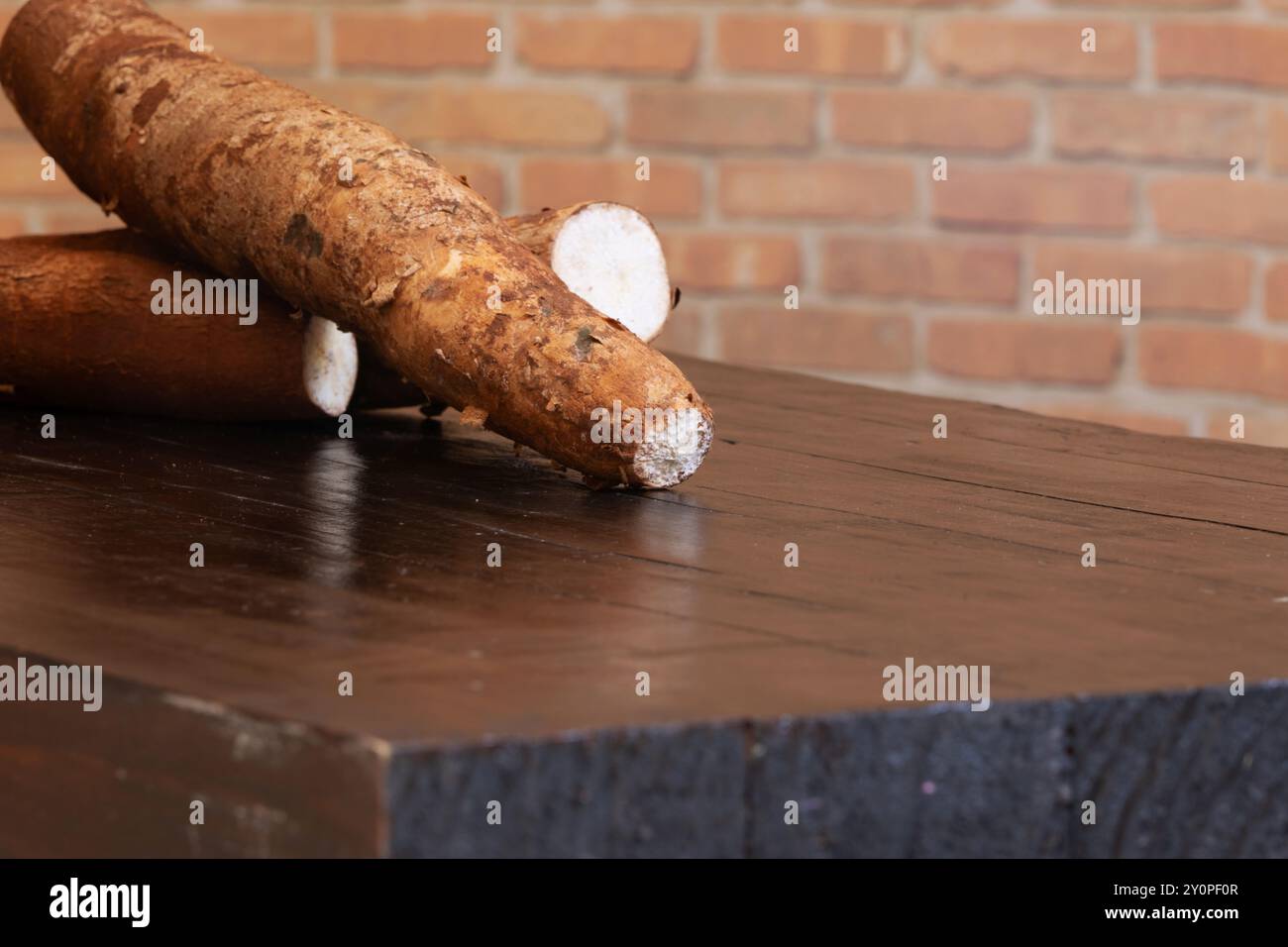 radici di manioca crude sopra un tavolo di legno scuro. Foto Stock