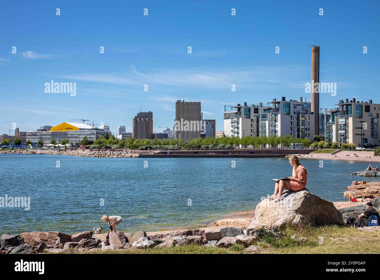 Donna seduta su una lettura di roccia a Eiran ranta nella soleggiata vigilia di mezza estate nel quartiere Eira di Helsinki, Finlandia Foto Stock