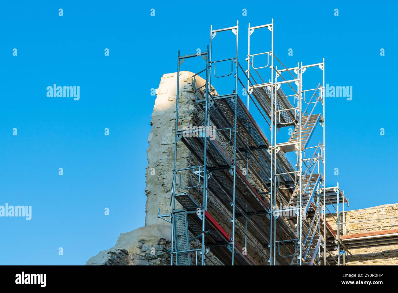 Una grande struttura a ponteggi supporta gli sforzi di restauro in corso su antiche rovine di pietra. Il cielo limpido offre uno sfondo luminoso mentre i lavoratori si preparano Foto Stock