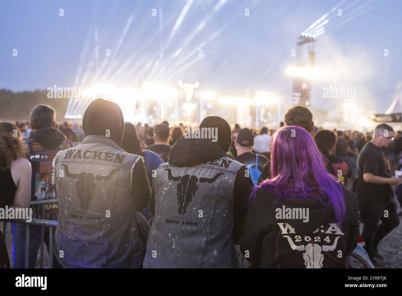 I visitatori del festival con giacche Wacken guardano i due palchi principali più velocemente e più duramente al crepuscolo al Wacken Open Air di Wacken. Il tradizionale metallo fe Foto Stock