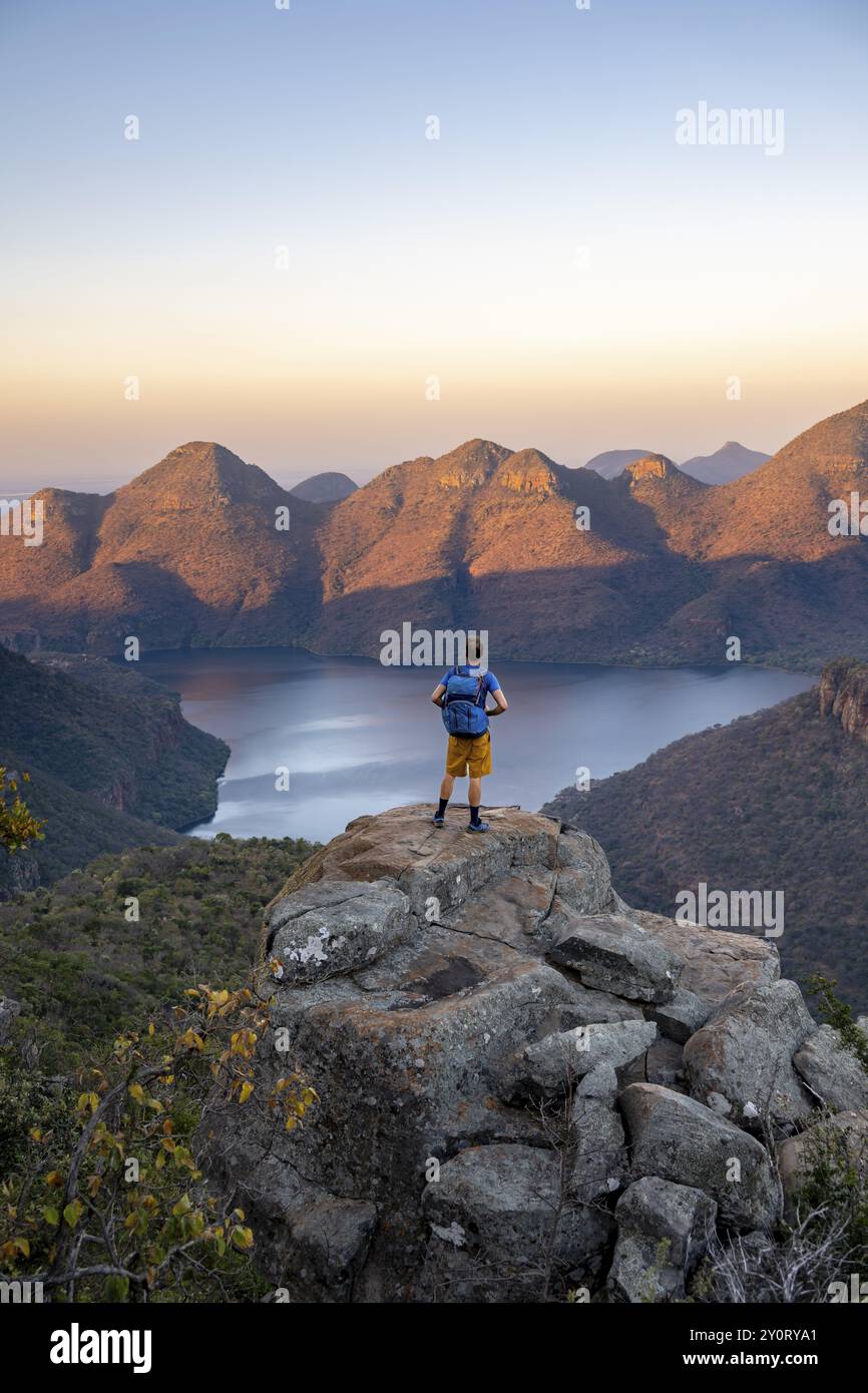 Giovane uomo in piedi sulle rocce e godendosi la vista, tramonto al Blyde River Canyon Vista del canyon con il fiume Blyde e le montagne da tavolo nella vita serale Foto Stock