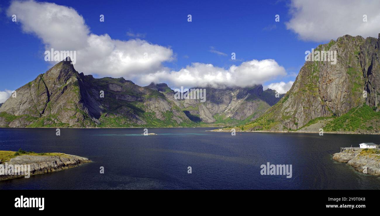 Imponenti montagne sotto un cielo blu con nuvole bianche accanto a un tranquillo fiordo, Reinefjord, Hamnoy, Moskenes Lofoten, Nordland, Norvegia, Europa Foto Stock