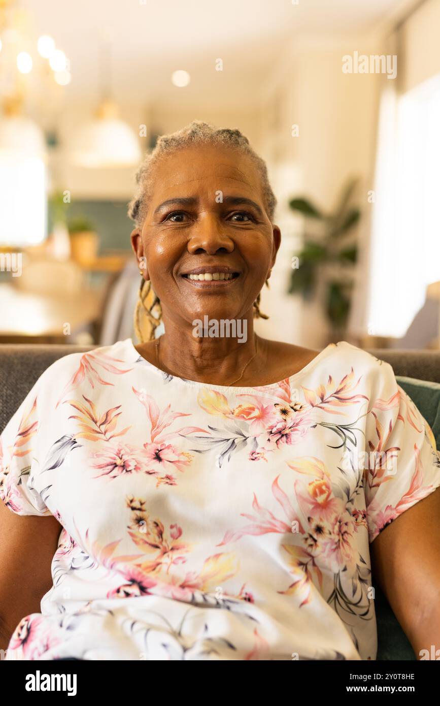 Donna anziana sorridente seduta sul divano di casa, godendo momenti di relax Foto Stock