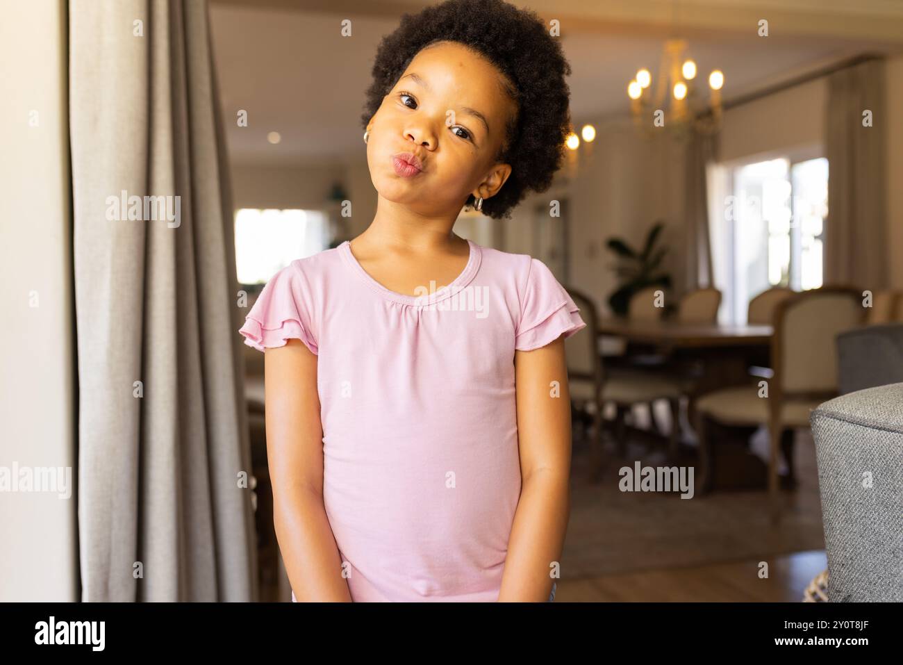 Ragazza sorridente in camicia rosa che posa giocosamente in un accogliente salotto di casa, spazio copia Foto Stock