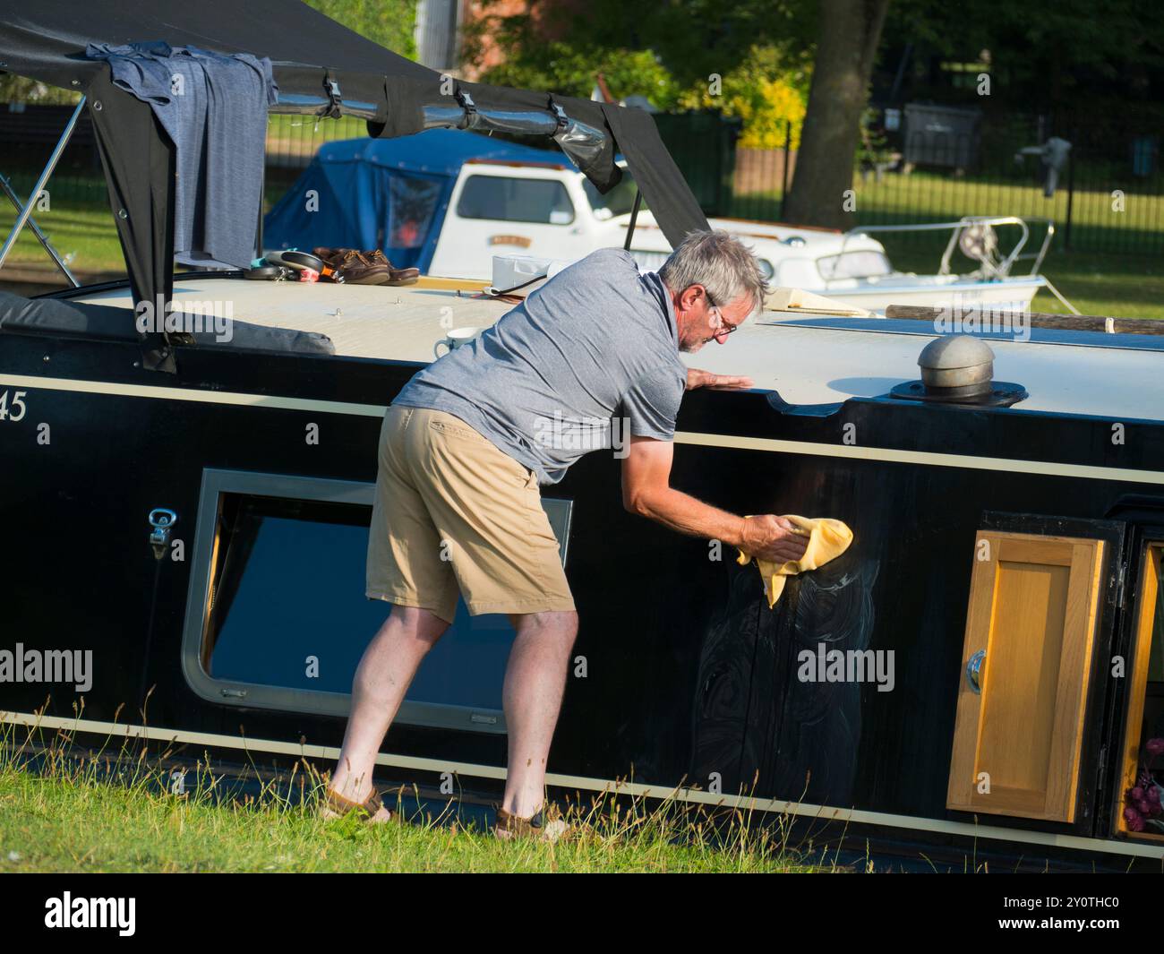 Proprietario orgoglioso di una casa galleggiante che pulisce la sua barca ormeggiata sul Tamigi ad Abingdon. Un rituale domenicale, proprio come lavare la tua auto... Siamo sulla sponda sud di TH Foto Stock