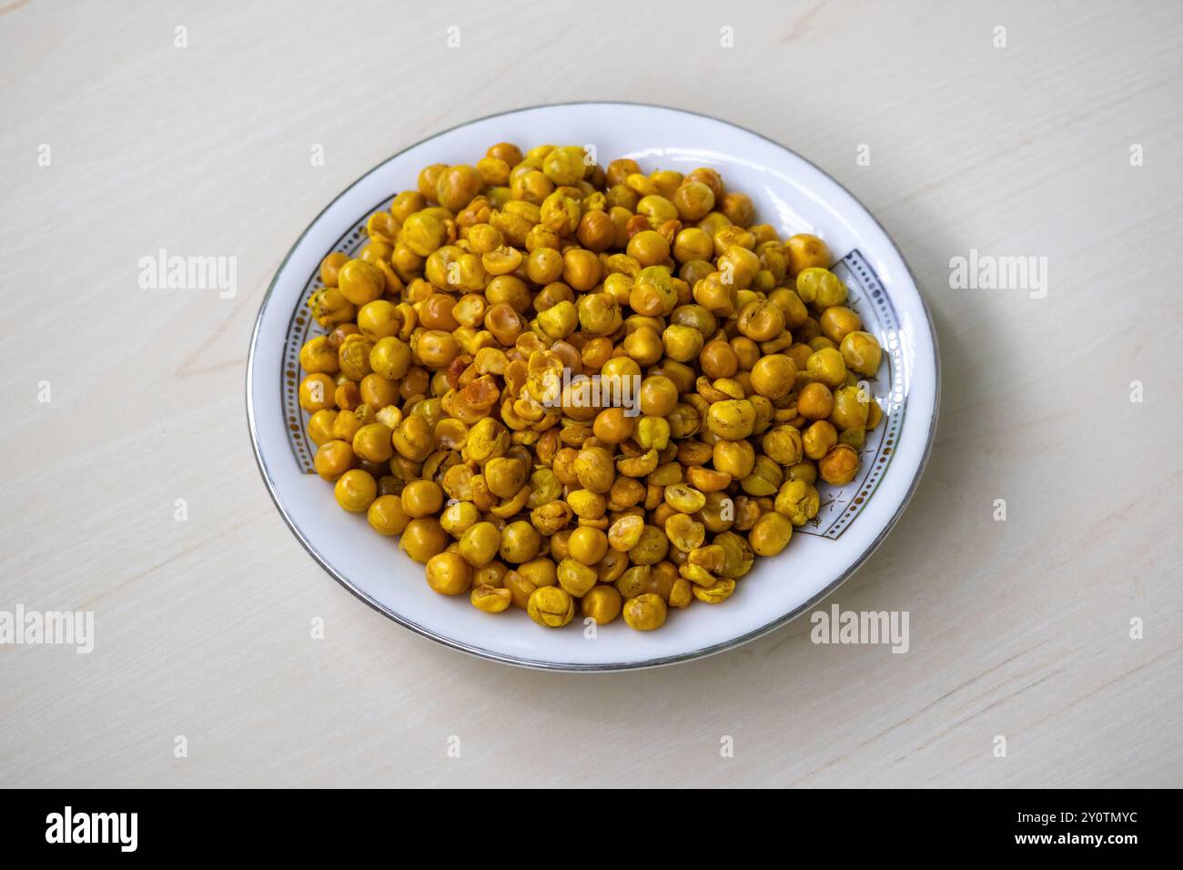 Piselli fritti piccanti su piatto bianco su superficie di legno. Delizioso spuntino conosciuto anche come dabli boot bhaja, piselli verdi piccanti, masala matar, hara matar Foto Stock