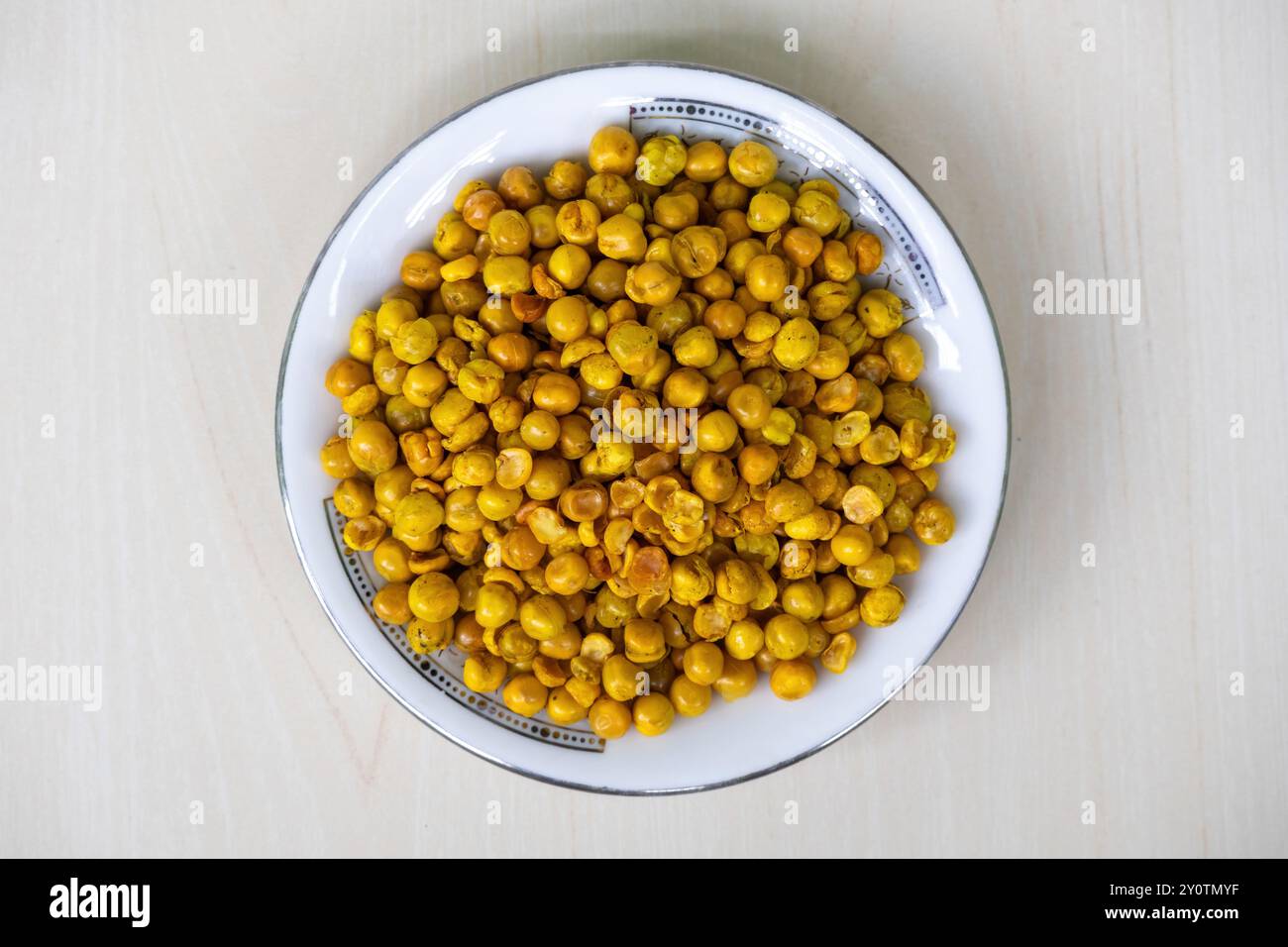 Piselli fritti piccanti su piatto bianco su superficie di legno. Delizioso spuntino conosciuto anche come dabli boot bhaja, piselli verdi piccanti, masala matar, hara matar Foto Stock