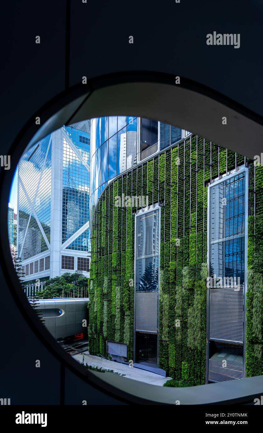 Vista di edifici moderni con un muro verde da una finestra circolare. Foto Stock