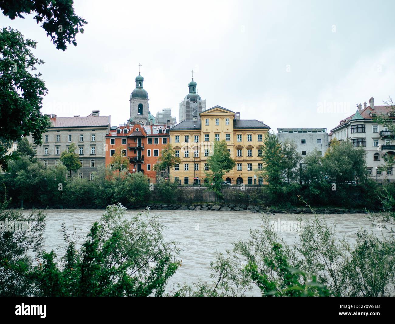 Una vivace vista sul fiume presenta una fila di edifici colorati completati da alberi, tutti adagiati contro un cielo nuvoloso, che creano un affascinante paesaggio urbano. Foto Stock