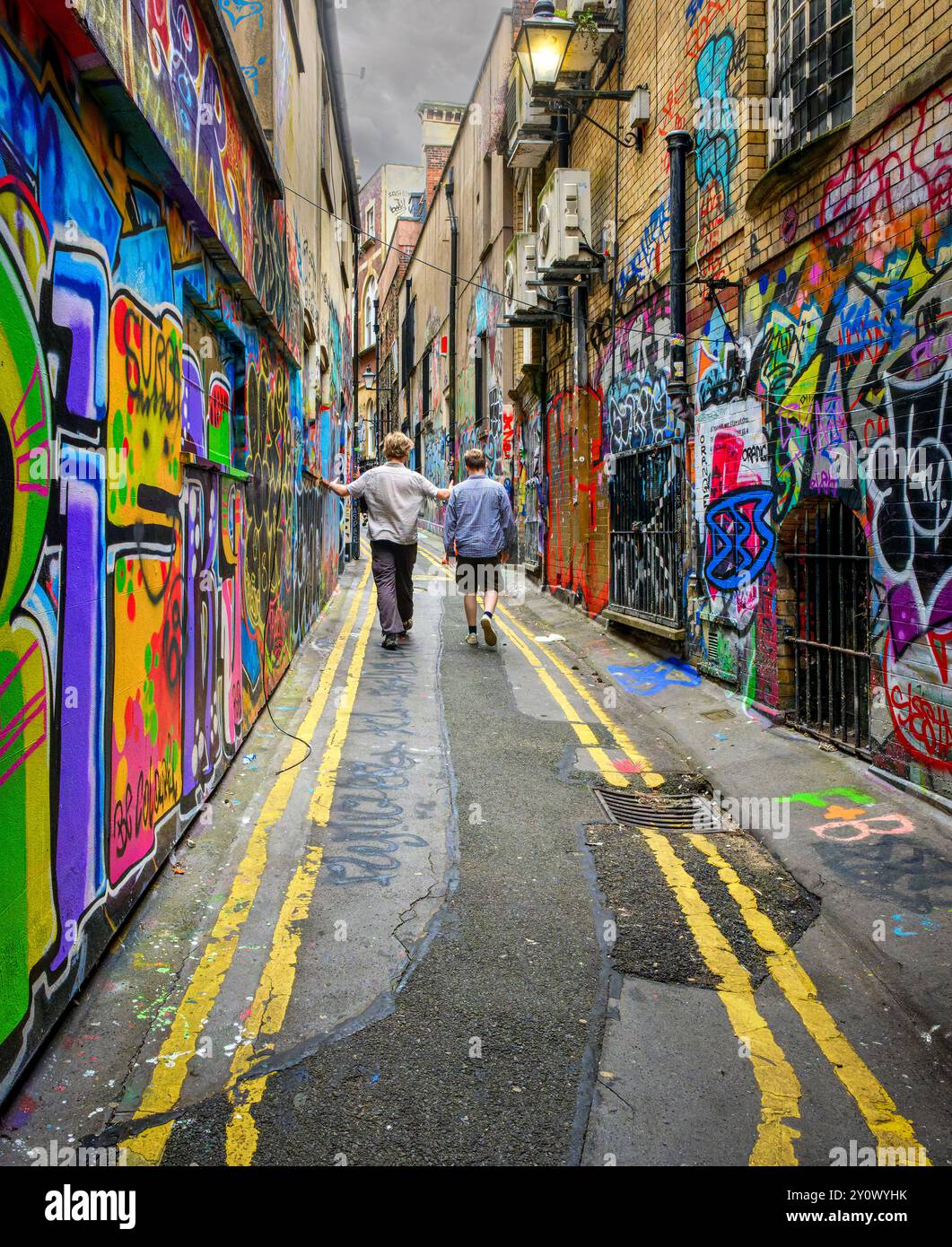 Due persone camminano lungo un vivace vicolo coperto di graffiti a Bristol Foto Stock