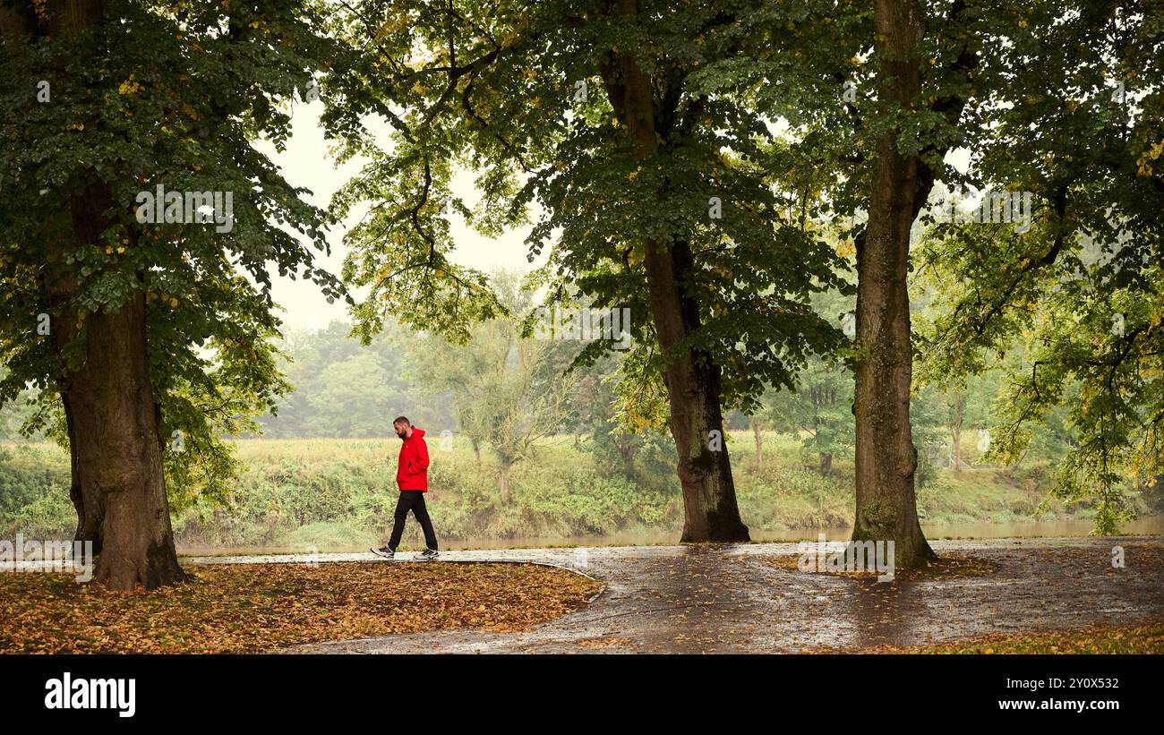 Uomo che indossa un cappotto impermeabile rosso che cammina lungo le rive del fiume Ribble a Preston Foto Stock Uomo che indossa un cappotto impermeabile rosso che cammina lungo le rive del fiume Ribble a Preston Foto Stock