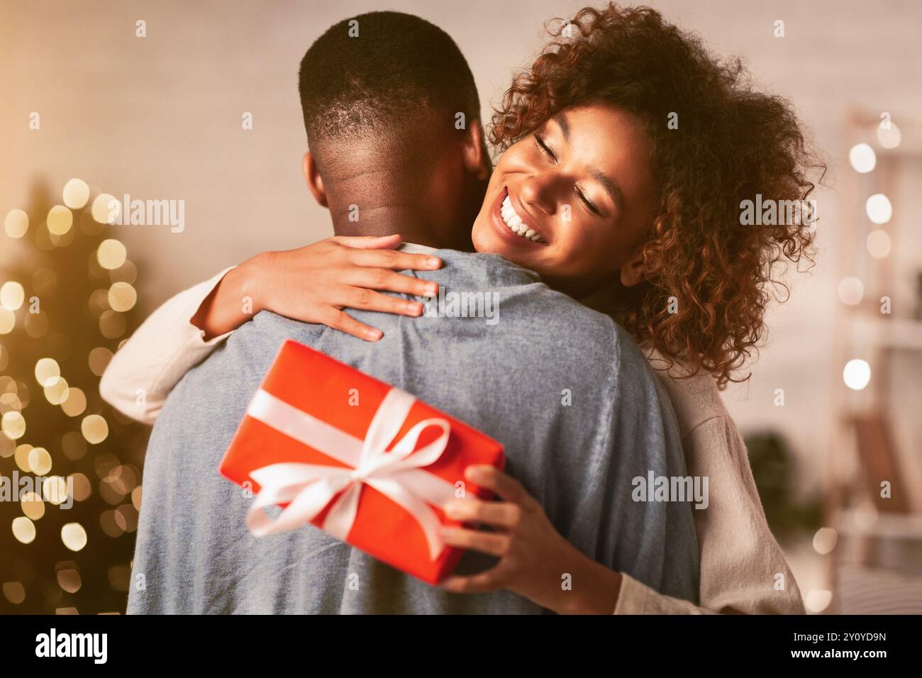 Grati afro donna con un regalo di Natale abbracciando il marito a casa Foto Stock
