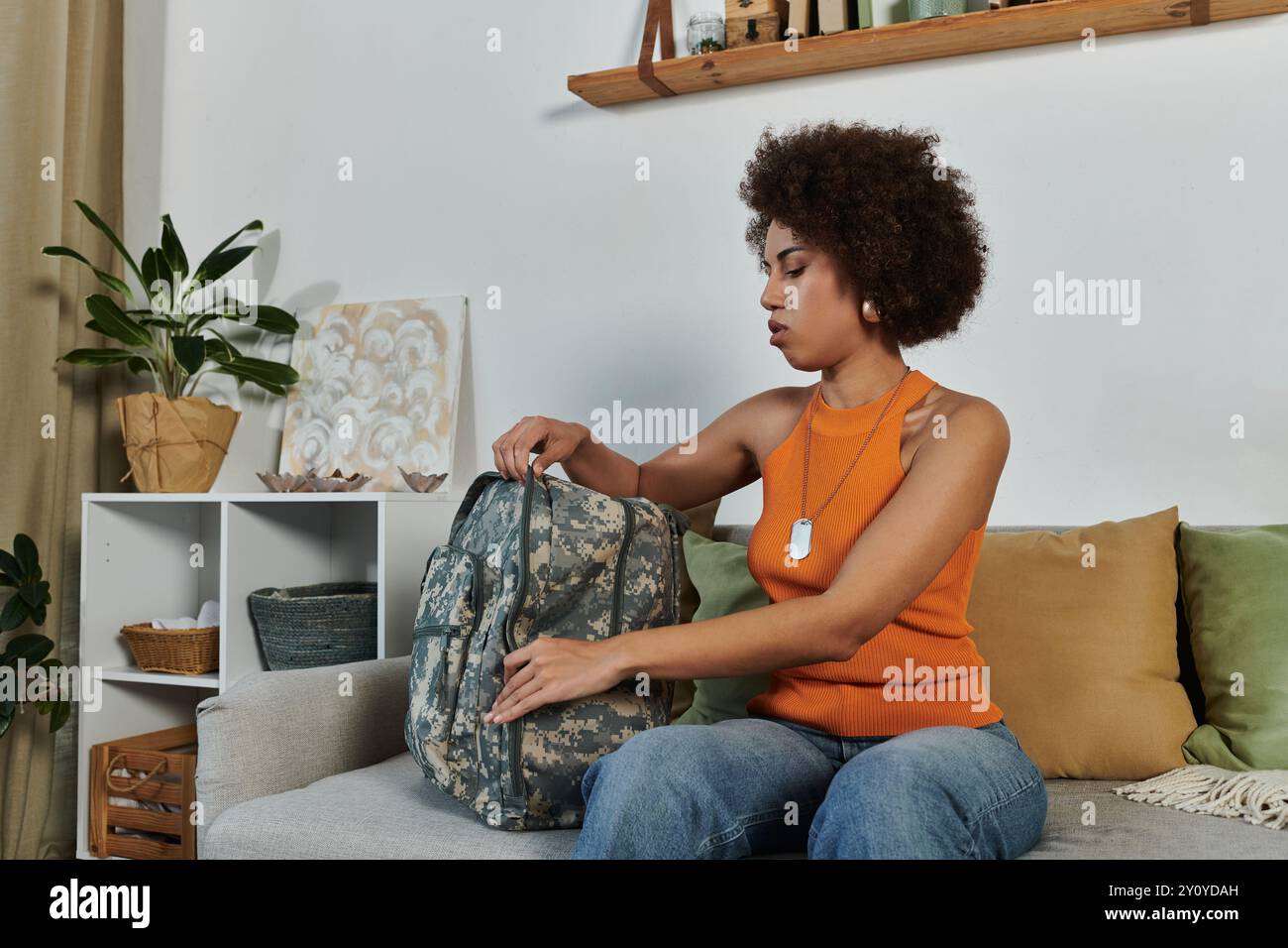 Una giovane donna afro-americana porta il suo zaino in un caldo soggiorno pieno di tocchi personali. Foto Stock