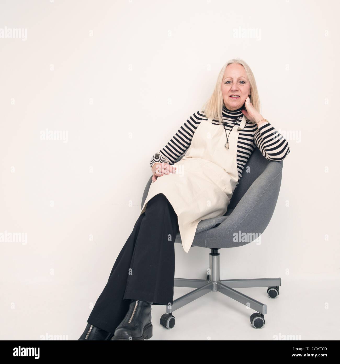 donna anziana che indossa il grembiule seduto su una sedia in studio Foto Stock