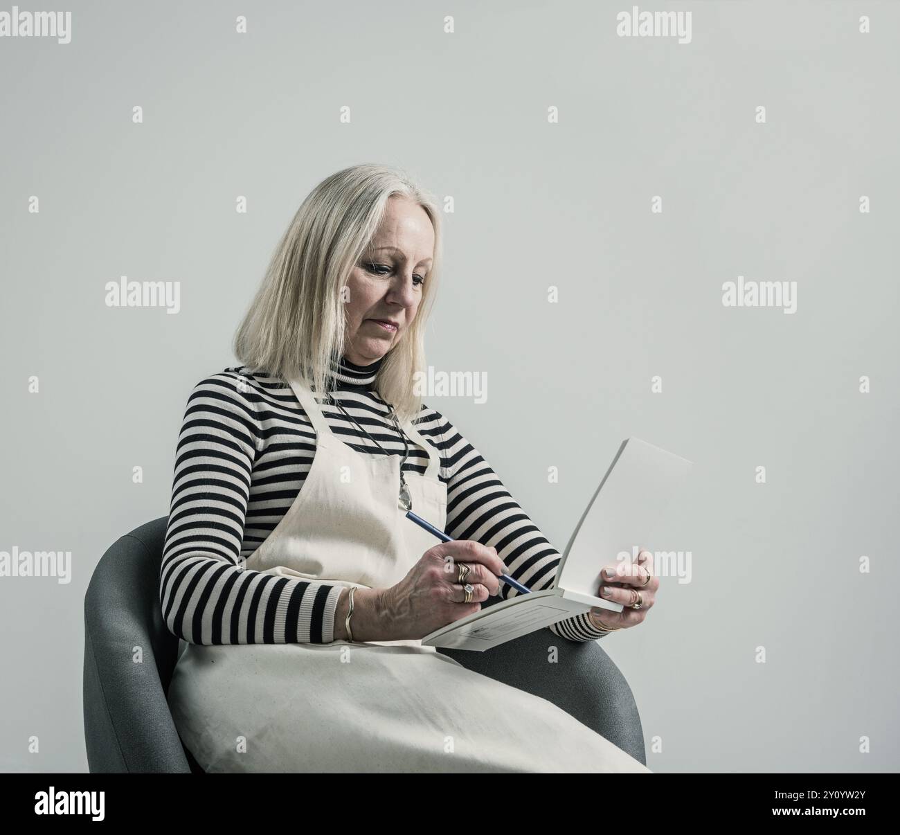donna anziana seduta e scrittrice su un notebook con grembiule Foto Stock