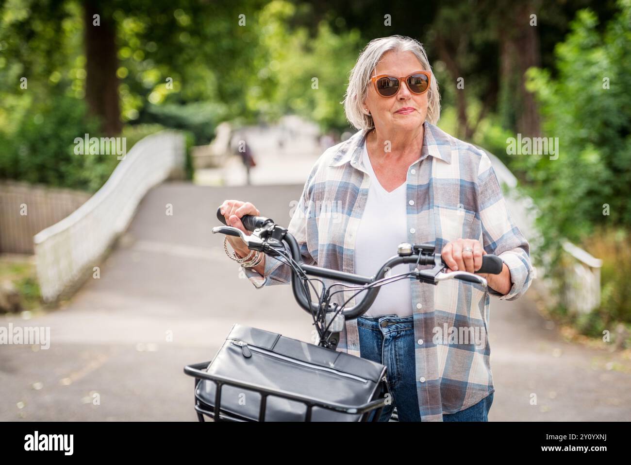 Donna anziana in sella a una bicicletta elettrica nel parco Foto Stock