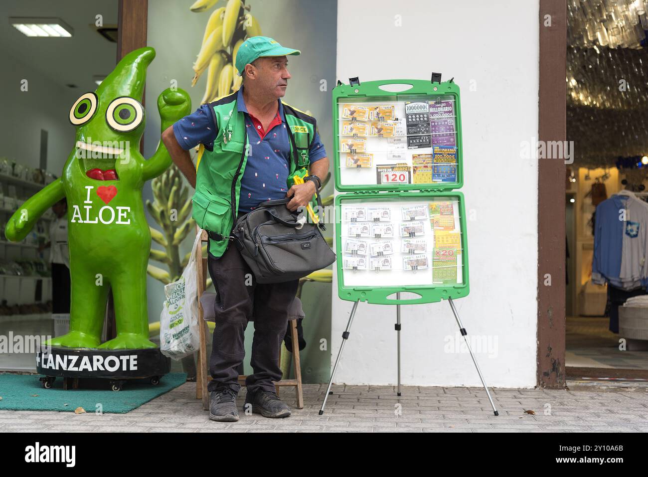 Spagna, Canarie, Lanzarote: Venditore di biglietti della lotteria spagnola in piedi fuori da un negozio con un grande cartello pubblicitario i Love Aloe. Foto Stock