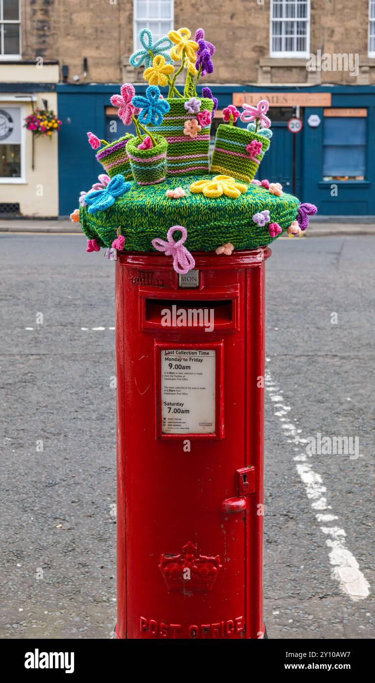 Copertura a maglia di vasi di fiori colorati sulla cassetta postale rossa Royal mail, Haddington High Street, Scozia, Regno Unito Foto Stock