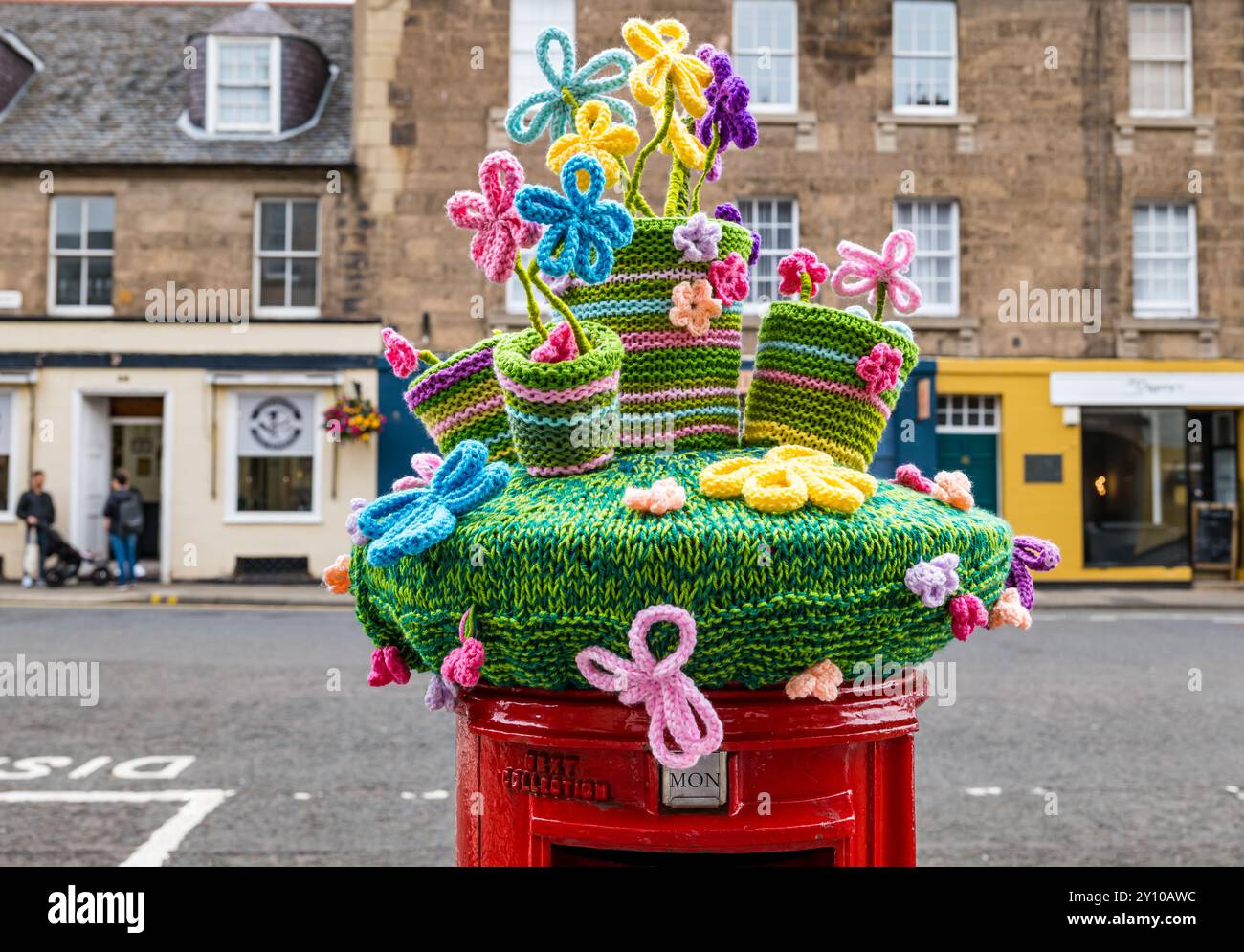 Copertura a maglia di vasi di fiori colorati sulla cassetta postale rossa Royal mail, Haddington High Street, Scozia, Regno Unito Foto Stock