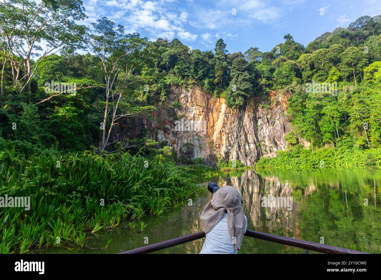 Vista posteriore di una donna con il velo, appoggiati al supporto, aspettando pazientemente di scattare una foto di uccelli selvatici in una riserva naturale di cava. Singapore. Foto Stock