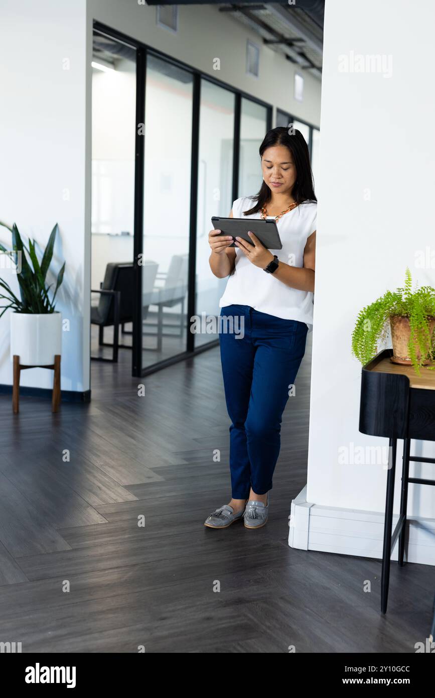 Con un tablet, una donna in piedi in un ufficio moderno vicino a una sala riunioni con pareti in vetro, spazio fotocopie Foto Stock