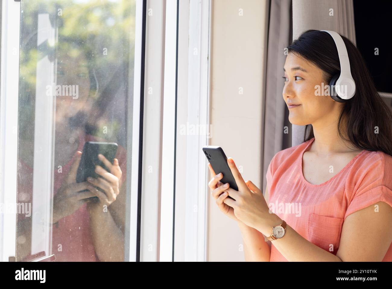 Ascolto di musica con le cuffie, donna asiatica che tiene in mano lo smartphone e guarda all'esterno, copia spazio Foto Stock