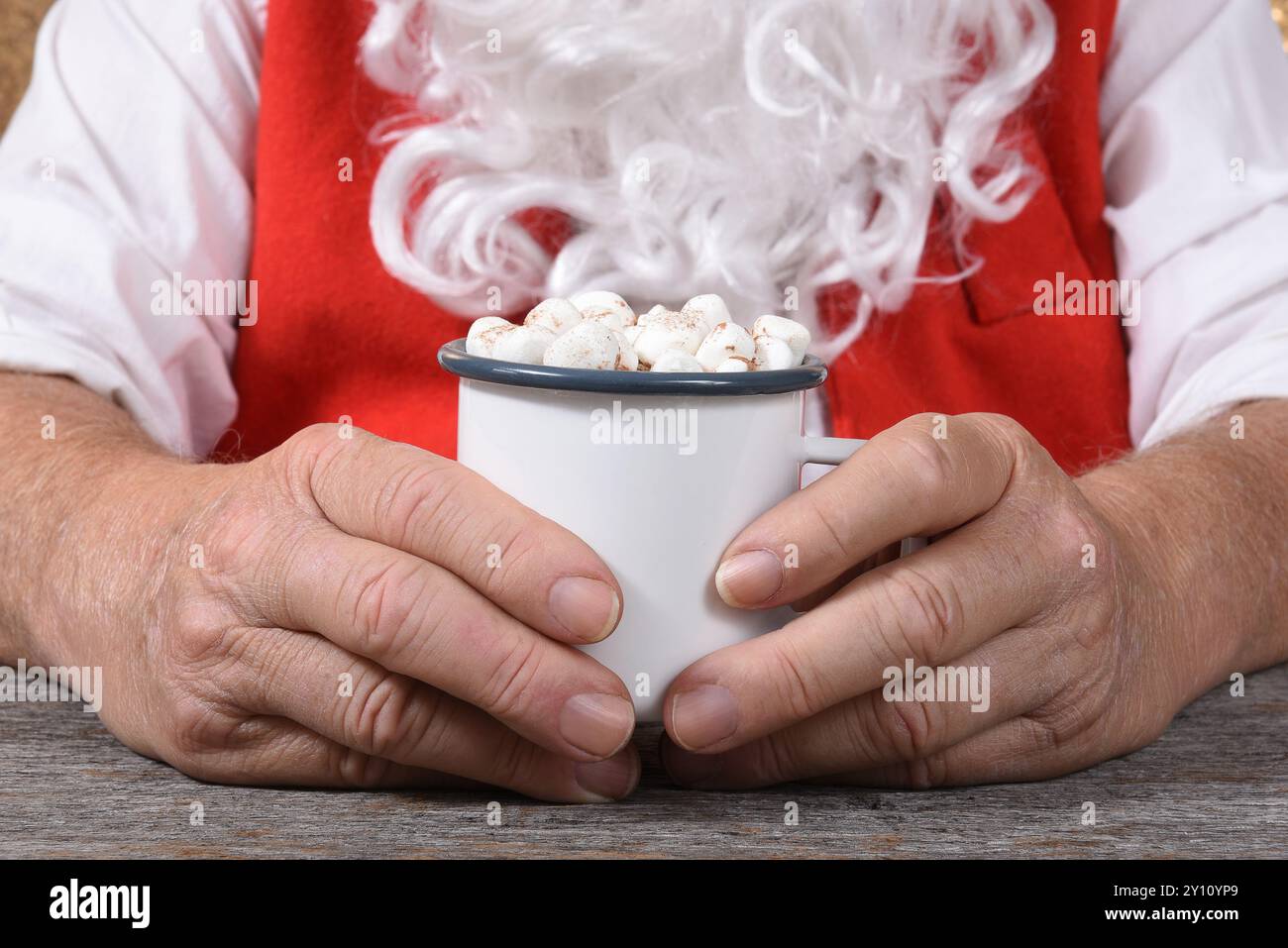 Primo piano di Babbo Natale con una tazza di cioccolata calda calda con marshmallow in entrambe le mani. Foto Stock