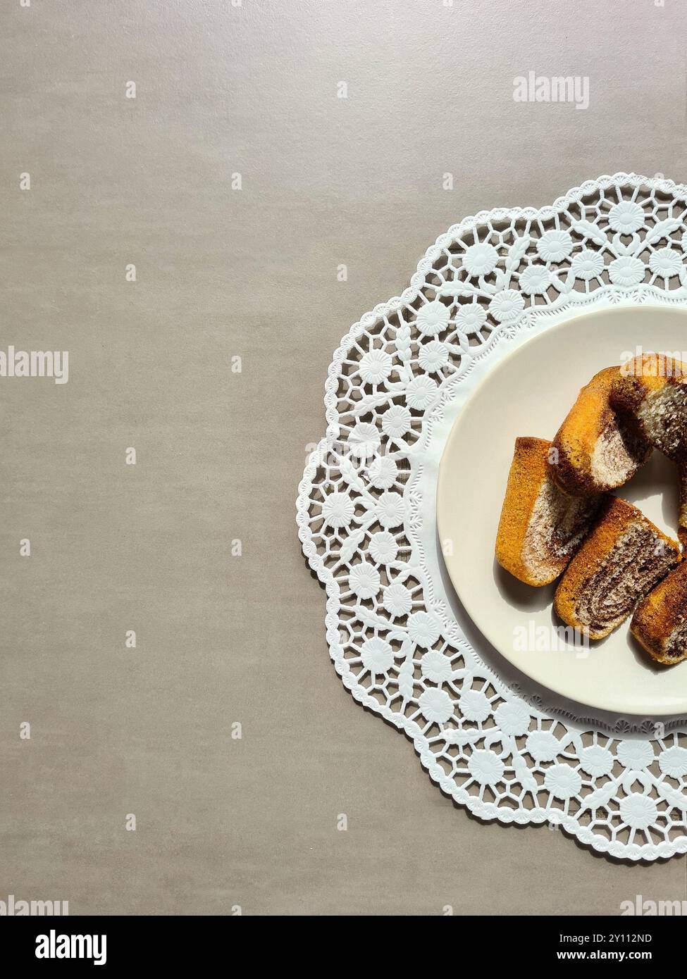 Pezzi singoli di torta di marmo serviti su un piatto bianco su un topper rotondo di carta decorativa su sfondo grigio Foto Stock