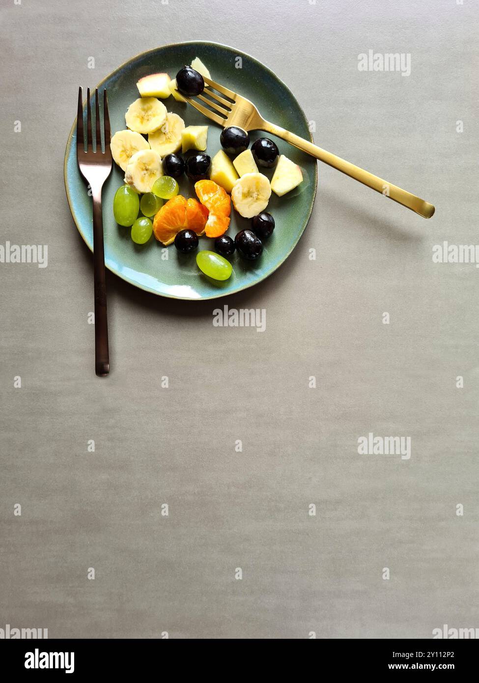Frutta fresca su un piatto blu-verde, nutrizione ricca di vitamine, diversi tipi di frutta fresca sana servita come Macedonia di frutta o spuntino con due forchette diverse Foto Stock