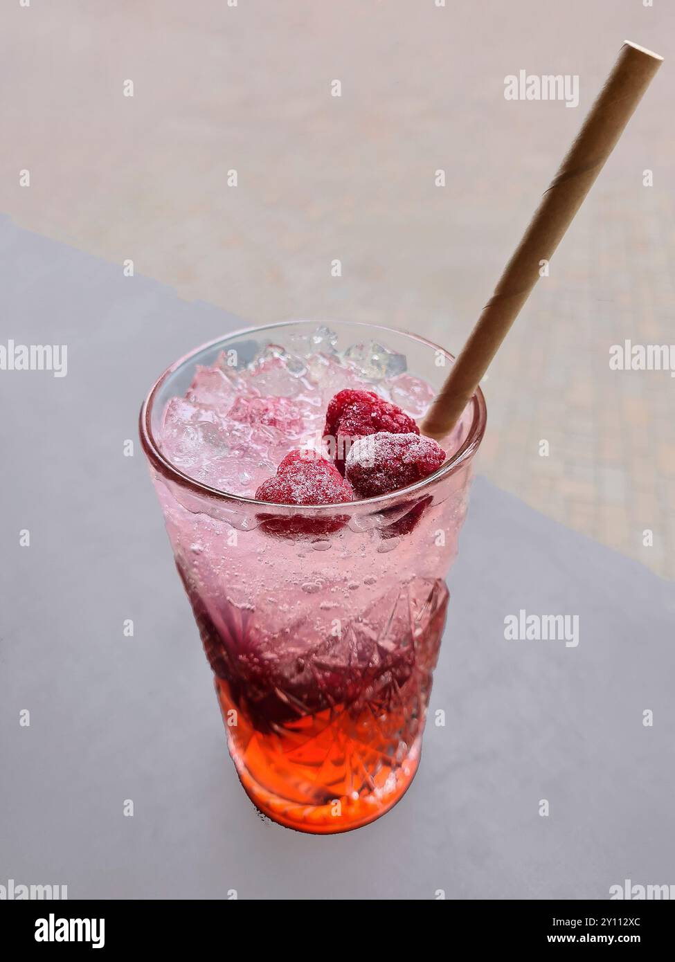 Una bevanda dissetante fruttata analcolica con una paglia e frutta in un bicchiere, rinfrescante in estate con una bevanda alla frutta rossa su ghiaccio Foto Stock