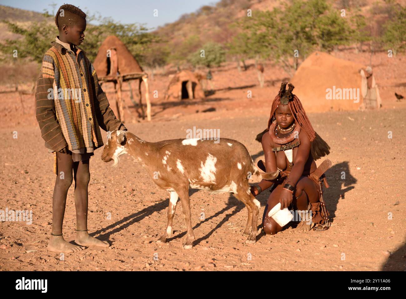 Giovane donna Himba e giovane che munge una capra, Kaokoveld, Namibia settentrionale, Namibia Foto Stock