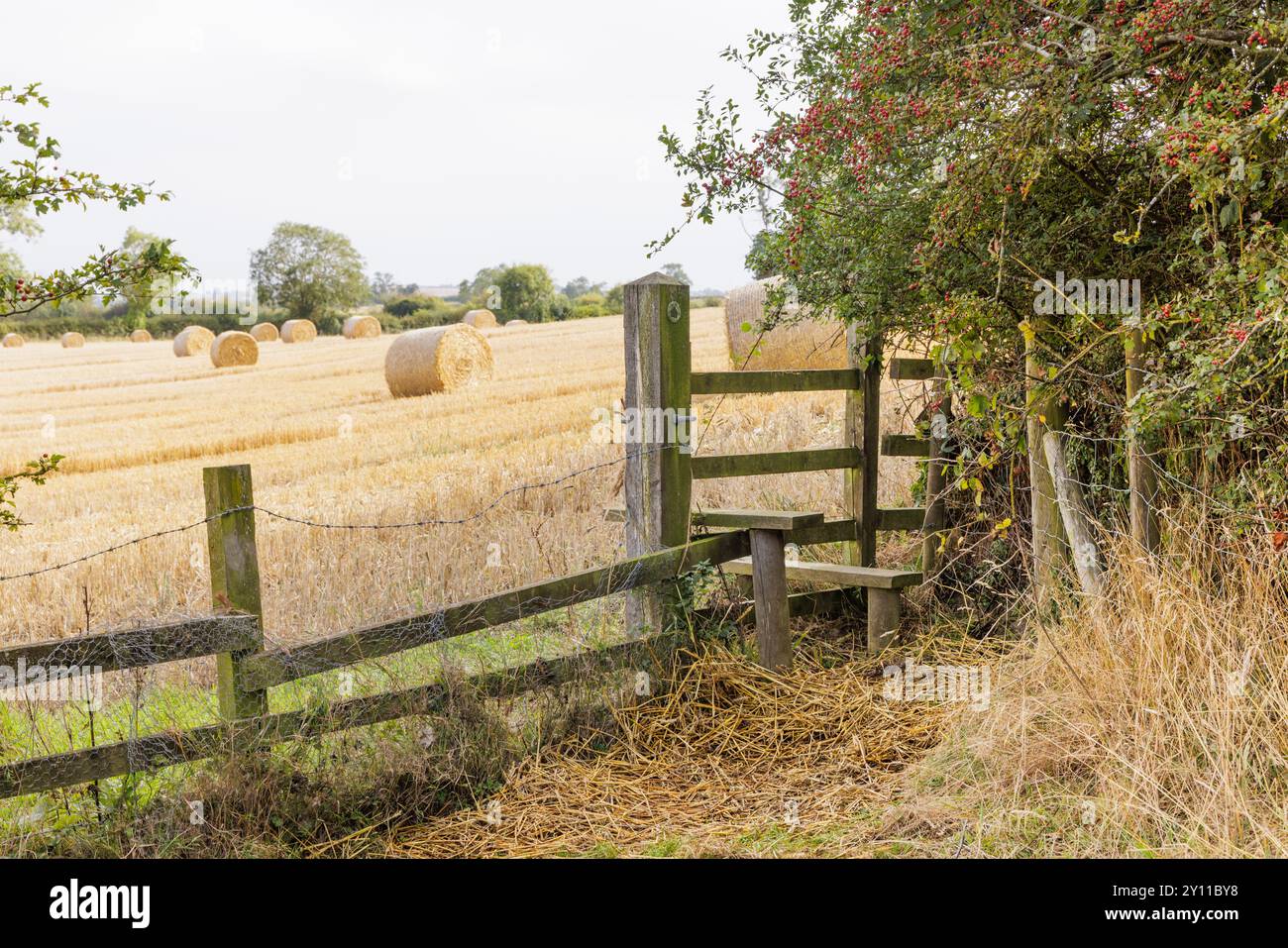 Fine estate - uno stile consente agli utenti del sentiero per Yelvertoft, Northamptonshire, di attraversare una recinzione di legno in un campo pieno di balle di fieno. Foto Stock