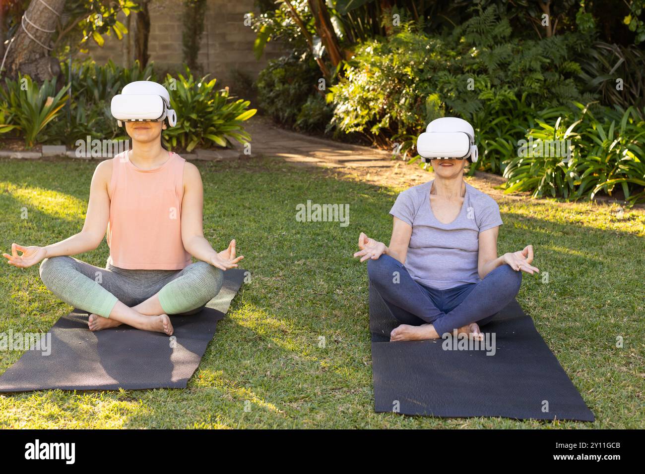 Pratica yoga su tappeti, nonna asiatica e nipote che indossano occhiali VR in giardino all'aperto Foto Stock