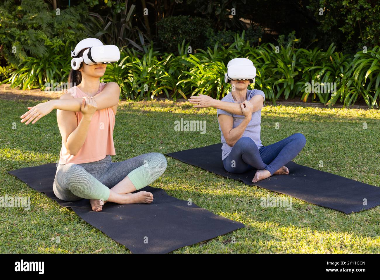 Utilizzando occhiali VR, nonna asiatica e nipote che si allungano su stuoie per yoga nel parco all'aperto Foto Stock