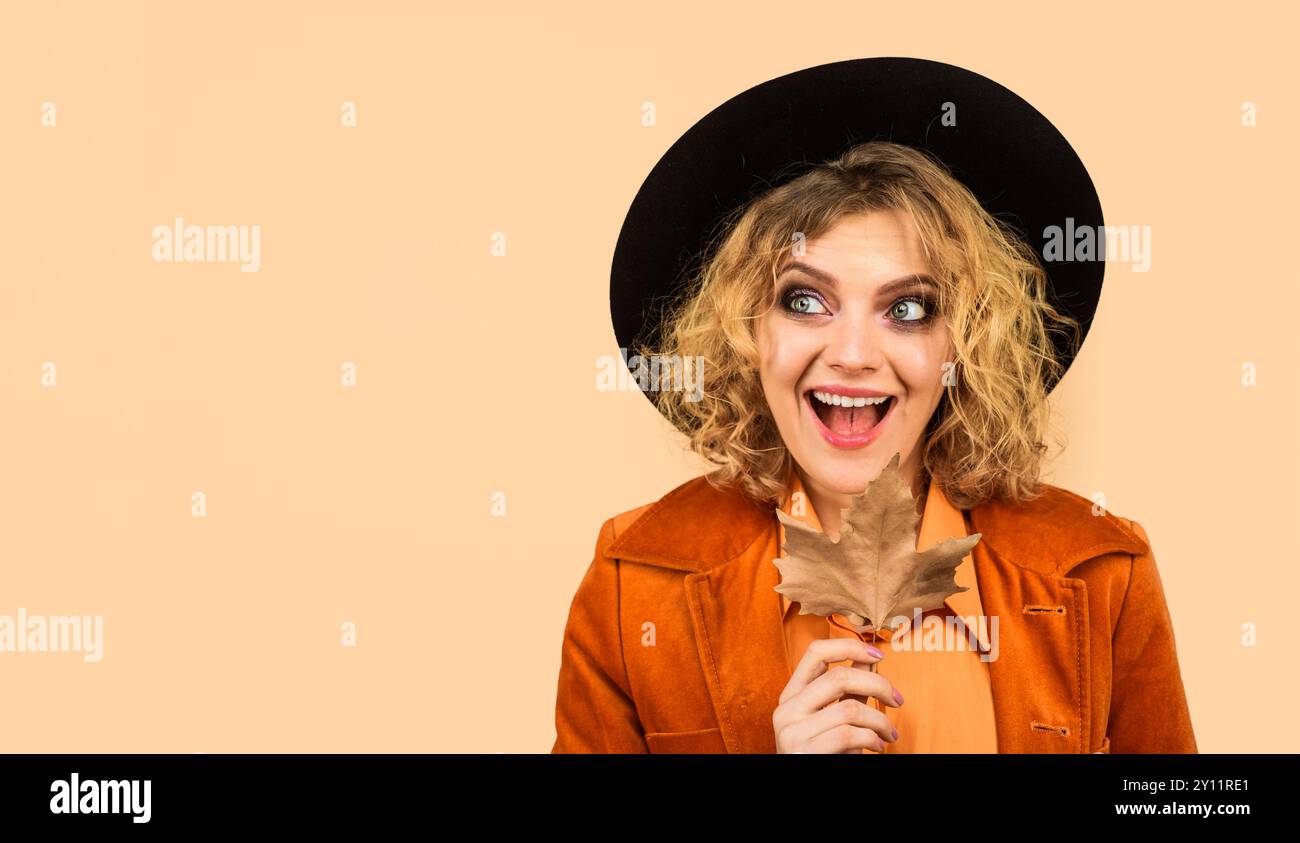 Donna felice in un outfit autunnale alla moda con foglie autunnali. Ragazza sorridente con elegante cappello nero e giacca alla moda con foglia d'acero. Donna autunnale con l'oro Foto Stock