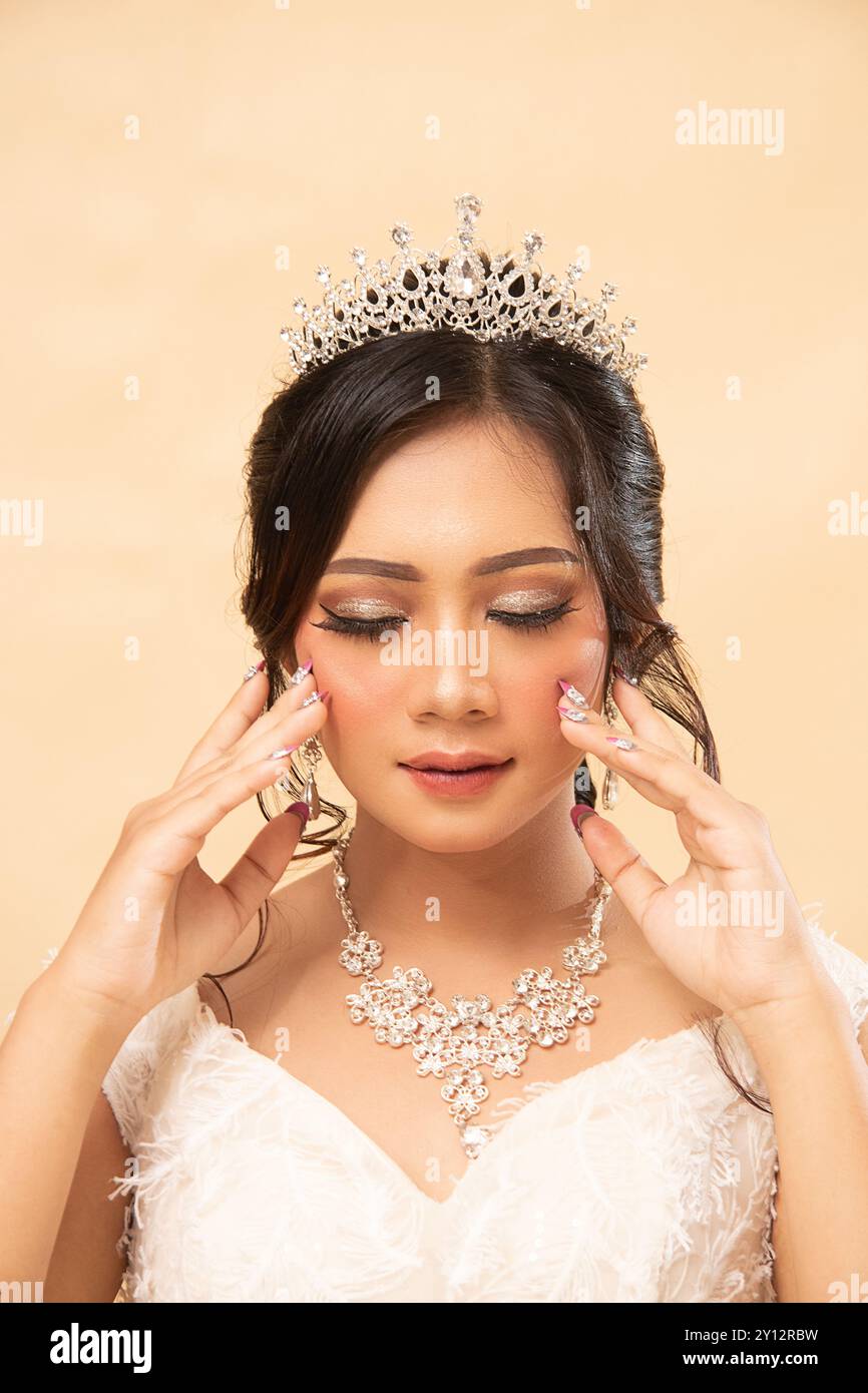 una donna di trucco seduta seduta formale rilassata e allegra che guarda lateralmente su per le scale tenendo le guance che chiudono gli occhi indossando un bellissimo vestito da foto al chiuso Foto Stock