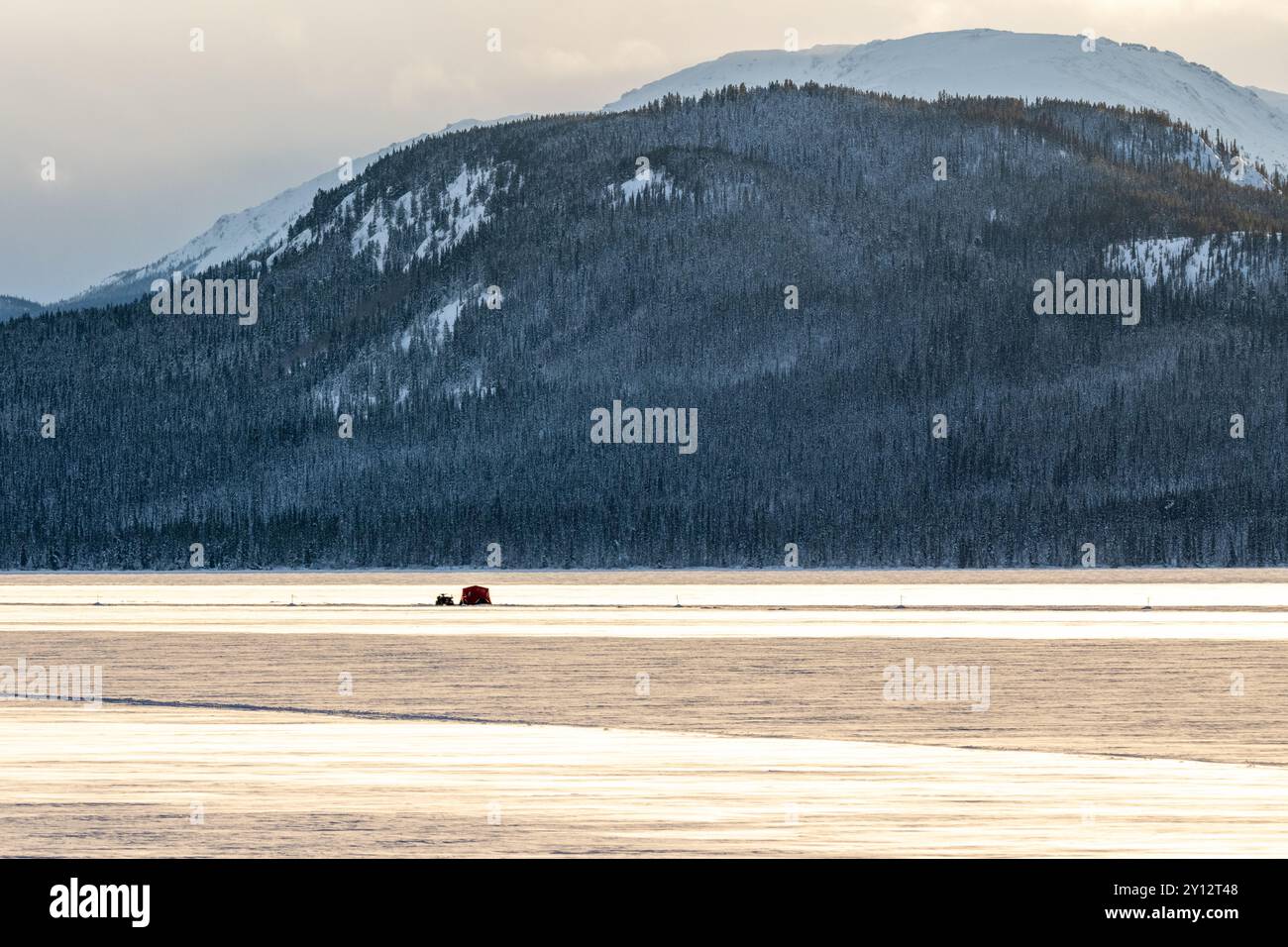 Vista sul lago ghiacciato nella natura selvaggia del Canada artico durante l'inverno, con lago ghiacciato, montagne innevate e capanne per la pesca sul ghiaccio. Foto Stock