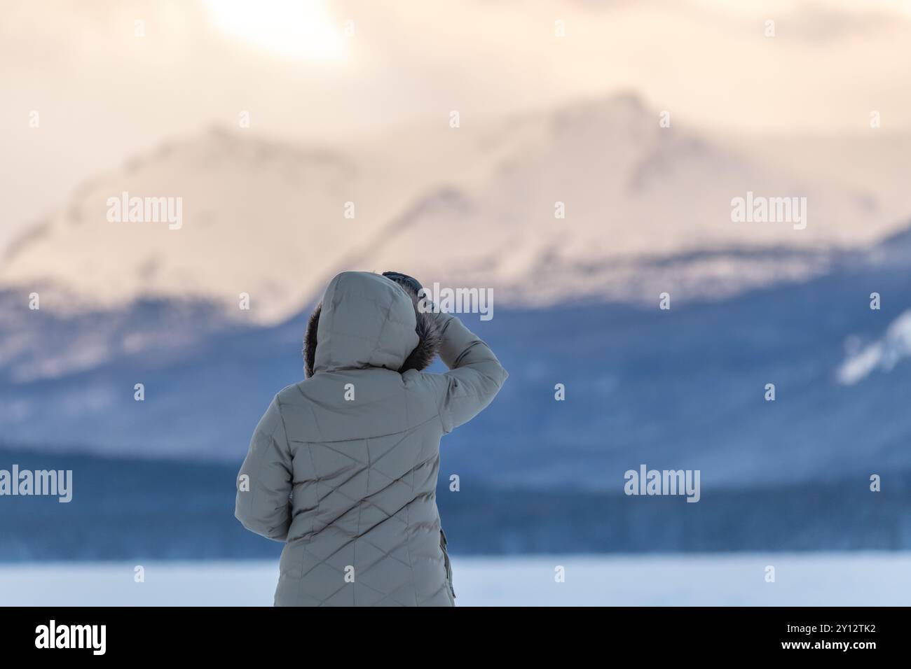 Sullo sfondo sono presenti montagne enormi e innevate, con donna vestita in pieno inverno e vestiti in primo piano sul lago ghiacciato. Foto Stock