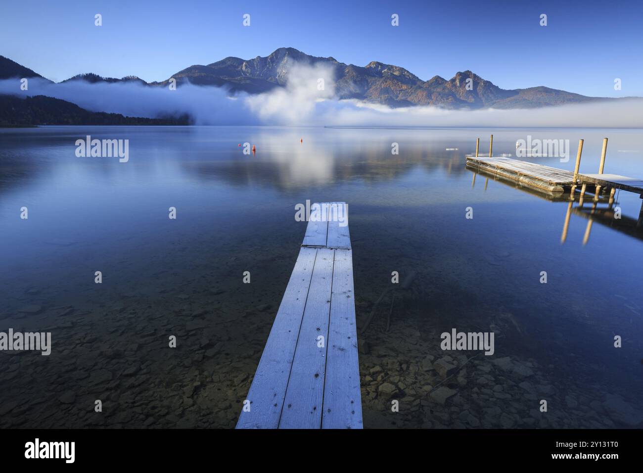 Atmosfera mattutina sul lago di montagna di fronte alle montagne, passerella, autunno, gelo, nebbia, riflessione, lago Kochel, vista su Herzogstand e Heimgarten Foto Stock