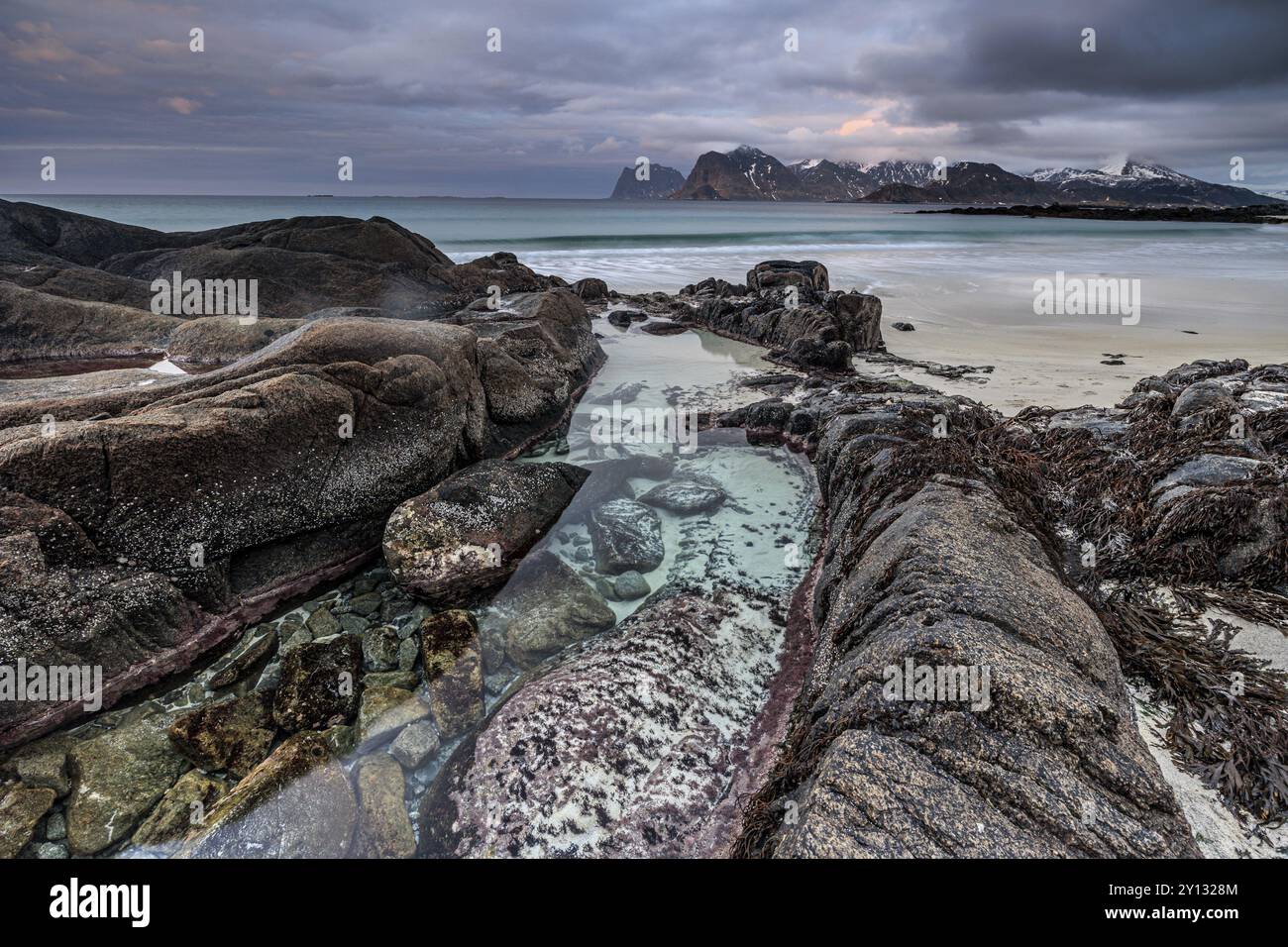 Rocce e spiaggia di fronte a Bergen, mare, surf, spruzzi, nuvole, inverno, Flakstadoya, Lofoten, Norvegia, Europa Foto Stock