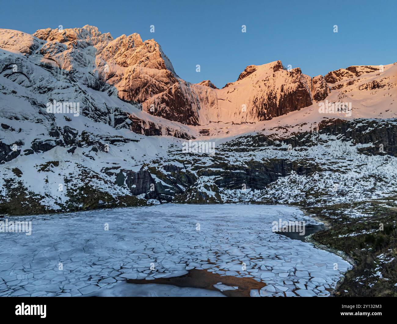 Vista aerea del lago ghiacciato di fronte a ripide montagne, inverno, alba, Storvatnet, Flakstadoya, Lofoten, Norvegia, Europa Foto Stock